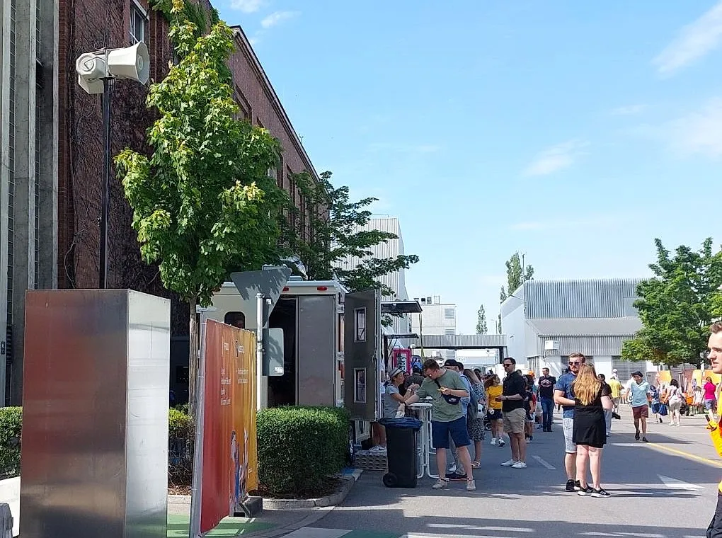 Besucher-Durchsage-System an einer Werksstraße während eines Firmenevents, im Hintergrund Besucher