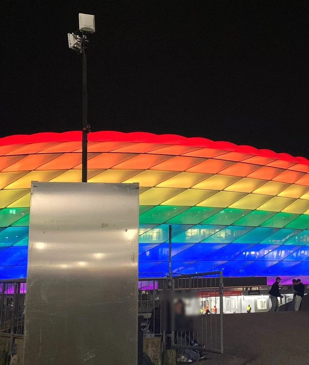 Mast mit Funkantennen und Technikschrank vor der beleuchteten Allianz Arena bei Nacht