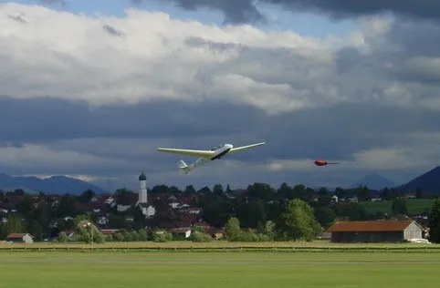 Segelflugzeug im Start über dem Flugplatz Königsdorf, dahinter Ort und Alpen