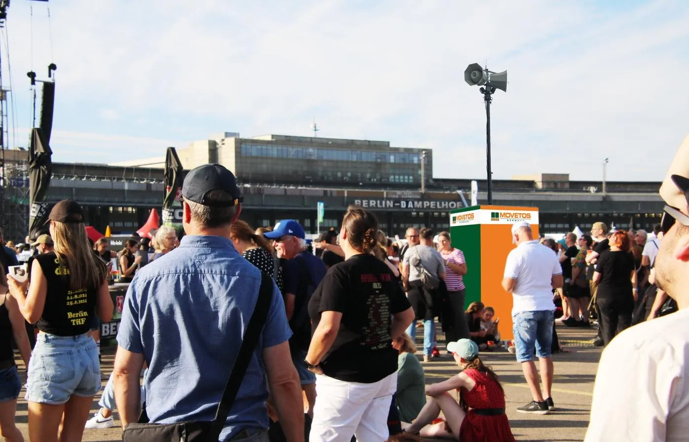 Konzertbesucher auf dem Tempelhofer Feld, dahinter ein Besucher-Durchsage-System in MOVETOS-Farben